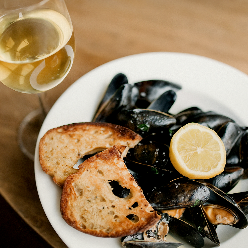 Mussels with lemon and bread on a plate, accompanied by a glass of white wine.